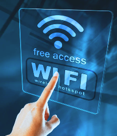 A left hand is pointing at a sign that reads "Free Access Wi-Fi." The finger is touching the letter "I" in the word "Wi-Fi." The sign includes the Wi-Fi symbol, followed by the words "Free Access," then "Wi-Fi," and finally "Wireless Hot Spot." All the text is inside a rounded border. The sign is displayed on a dark blue glass surface.