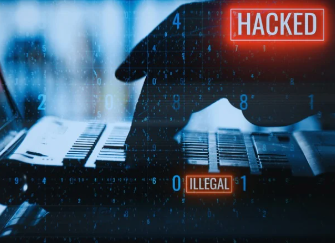 A close-up image shows fingers typing on a laptop keyboard. Above the keyboard, the word "HACKED" appears in large white letters with a red border, looking like a warning alert. Nearby, the word "ILLEGAL" is also framed in red at a different angle, emphasizing the danger of cyberattacks.