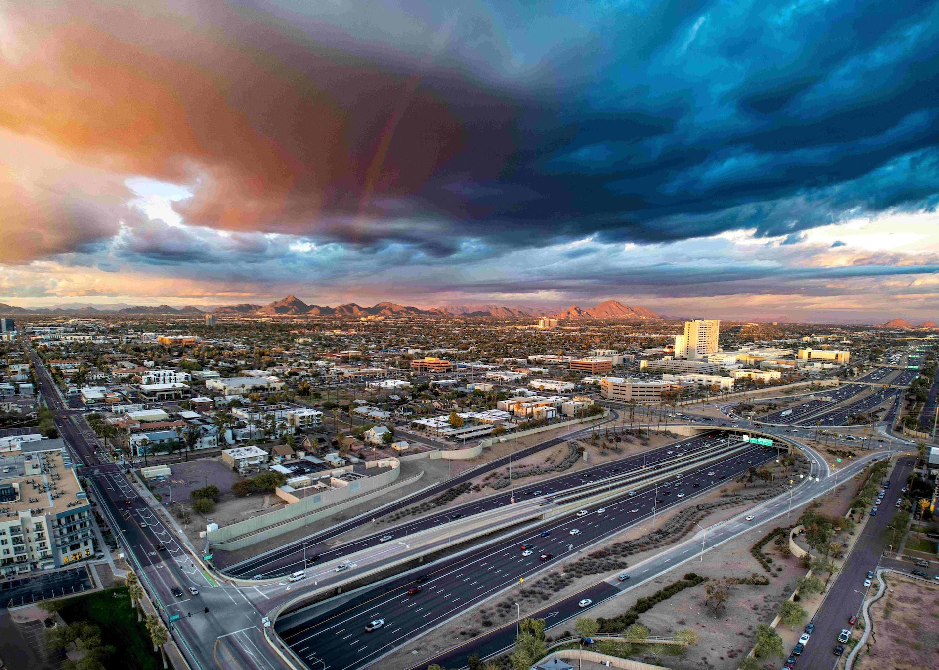 Arial photograph of the City of Phoenix,  with a highway in the foreground and mountains in the far background.