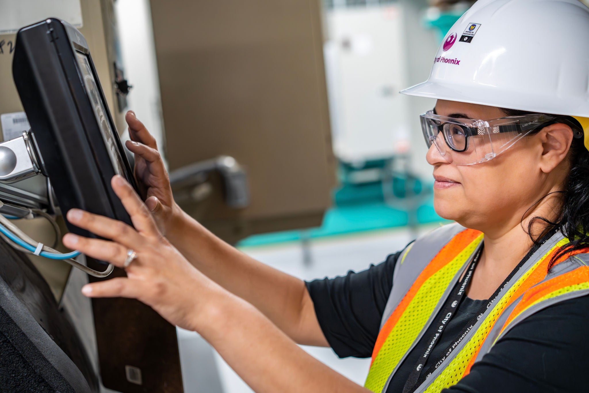 A building equipment operator in a hard hat works with an HVAC system in a mechanical room