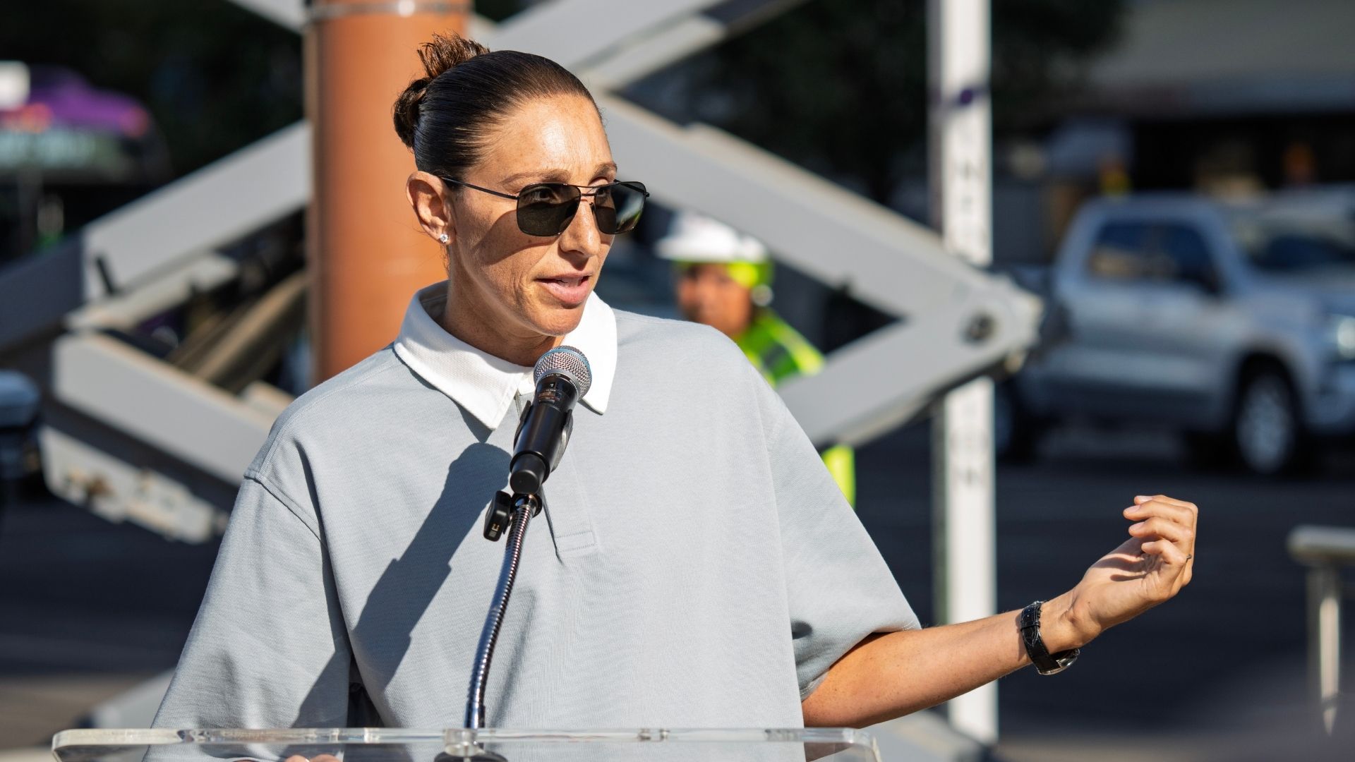 WNBA legend Diana Taurasi, wearing a gray shirt, speaking in front of a microphone.