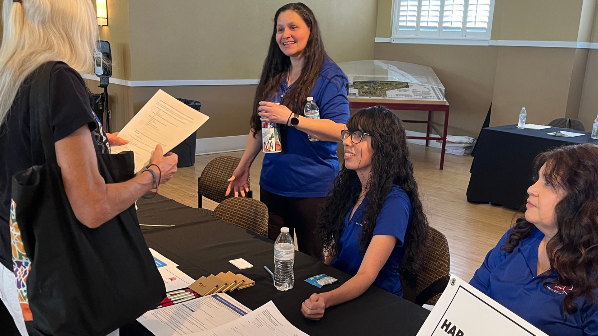 Three women working the Landlord Open House speak to a resident at a table with information about the Housing Choice Voucher program and HAP Contracts. 